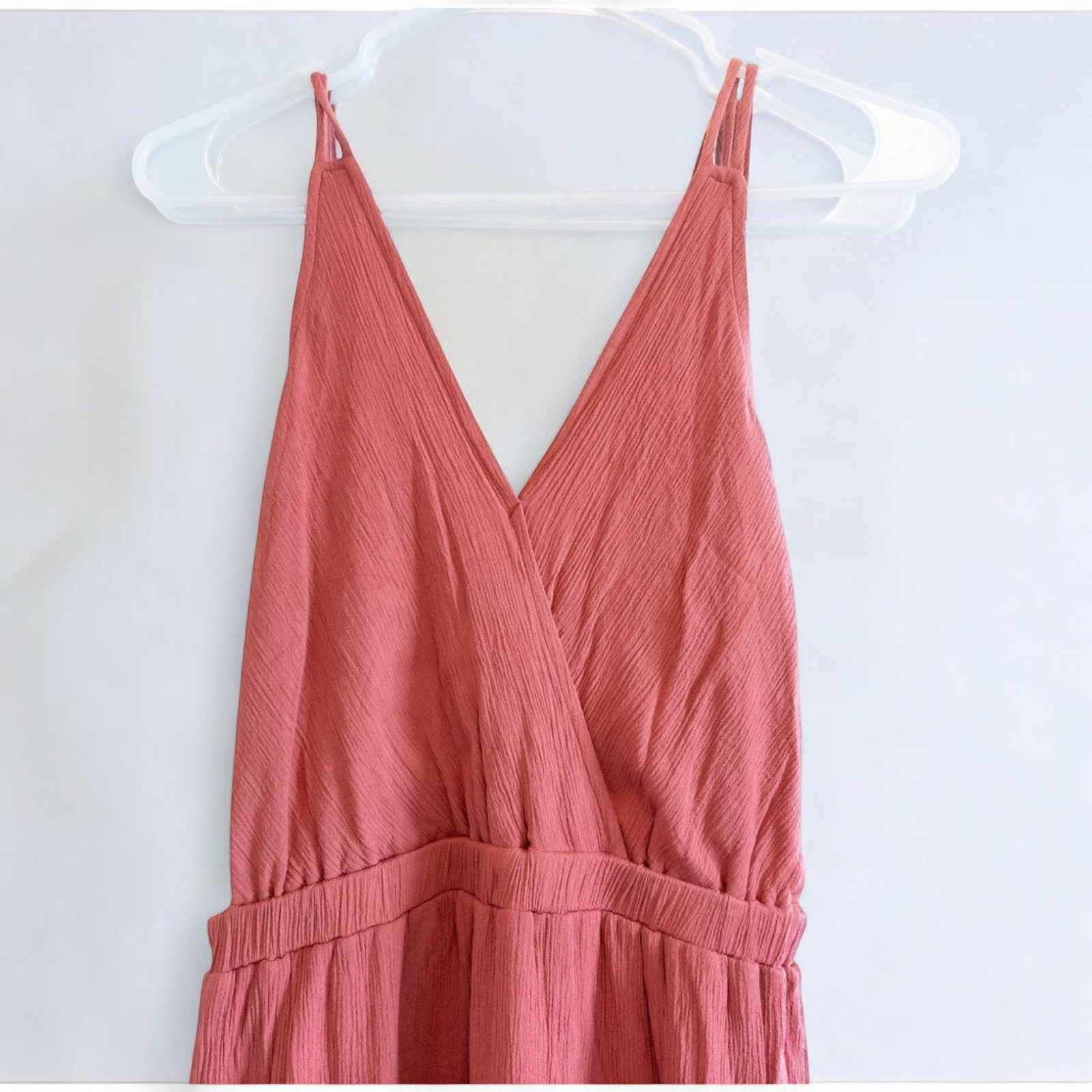 Pink sleeveless maxi dress with v-neckline and open back hanging on plastic hanger in front of mirror image 4