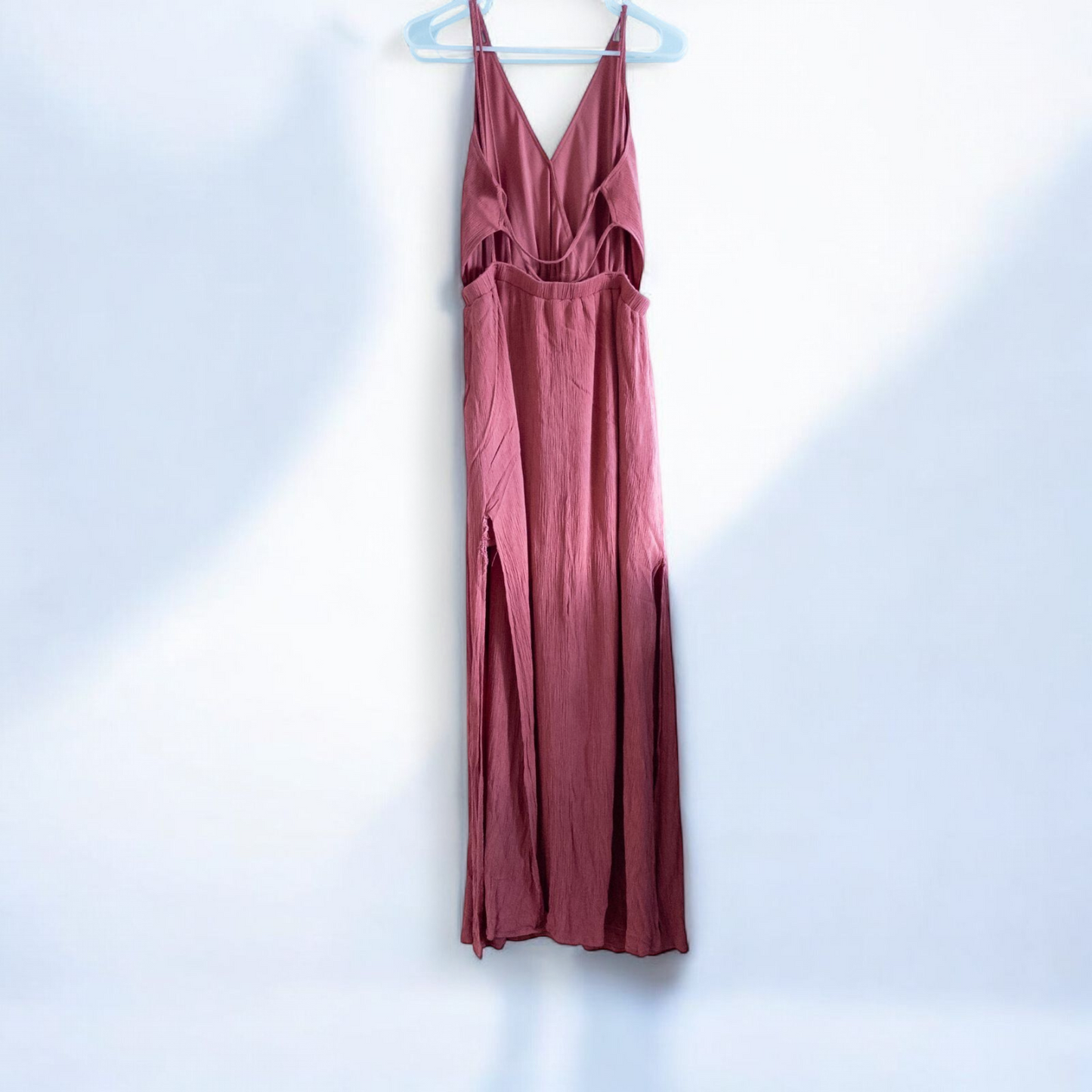 Pink sleeveless maxi dress with v-neckline and open back hanging on plastic hanger in front of mirror image 6
