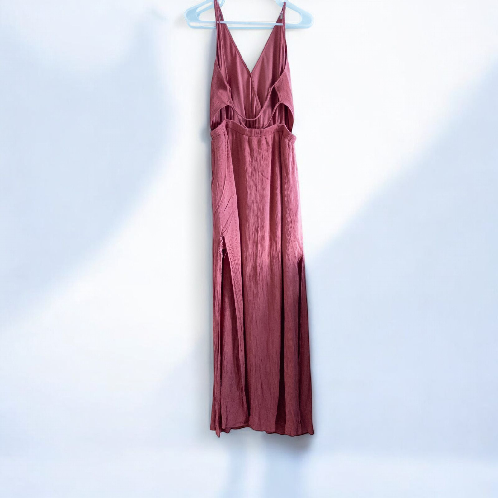 Pink sleeveless maxi dress with v-neckline and open back hanging on plastic hanger in front of mirror image 6