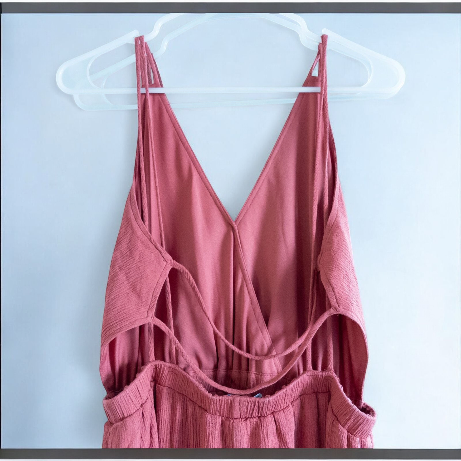Pink sleeveless maxi dress with v-neckline and open back hanging on plastic hanger in front of mirror image 7