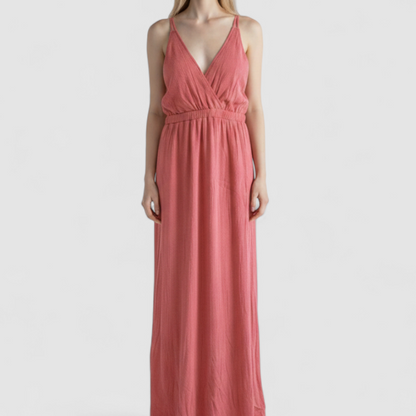 Pink sleeveless maxi dress with v-neckline and open back hanging on plastic hanger in front of mirror on model