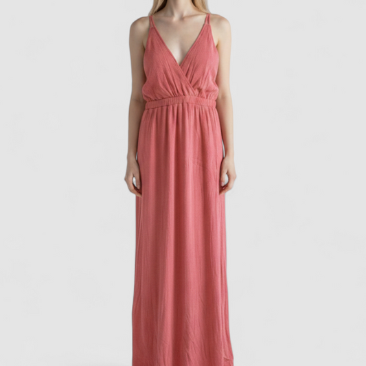 Pink sleeveless maxi dress with v-neckline and open back hanging on plastic hanger in front of mirror on model