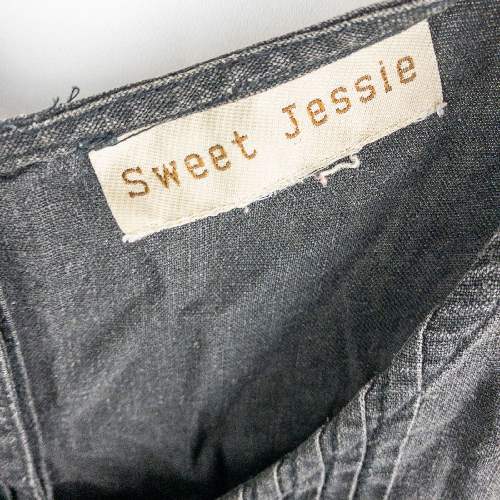 Sweet Jessie black denim long sleeveless dress with front decorative buttons and back button closure hanging on a hanger in front of a bookshelf and mirror image 10