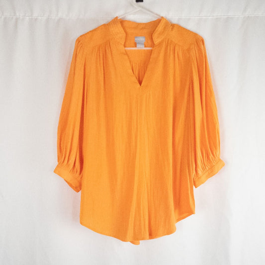 Bright orange long sleeve tunic blouse by Chicos hanging on a white hanger, showing front, back, sleeves, and fabric texture with small pinprick flaw