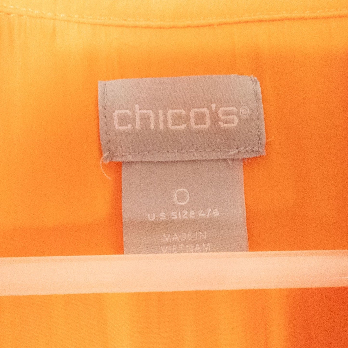 Bright orange long sleeve tunic blouse by Chicos hanging on a white hanger, showing front, back, sleeves, and fabric texture with small pinprick flaw image 7
