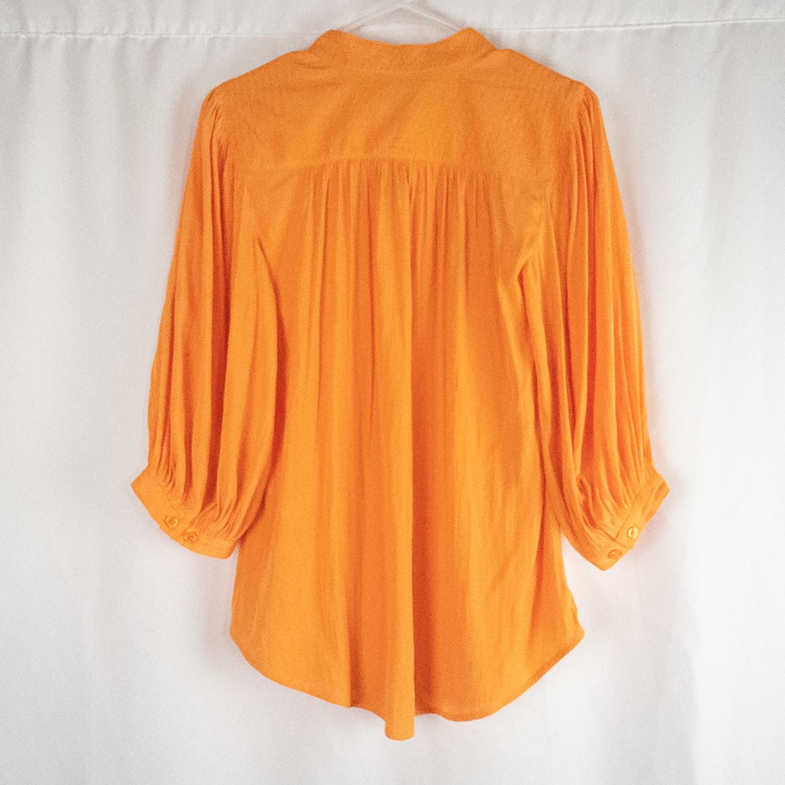 Bright orange long sleeve tunic blouse by Chicos hanging on a white hanger, showing front, back, sleeves, and fabric texture with small pinprick flaw image 5