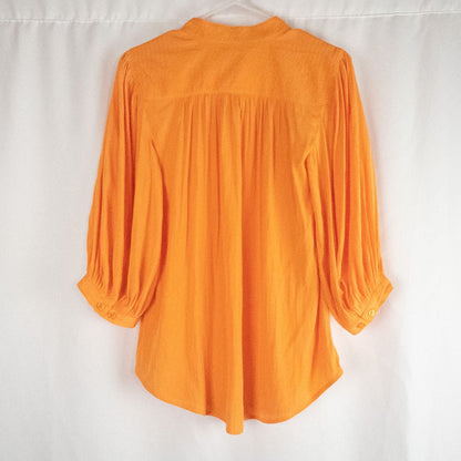 Bright orange long sleeve tunic blouse by Chicos hanging on a white hanger, showing front, back, sleeves, and fabric texture with small pinprick flaw image 5