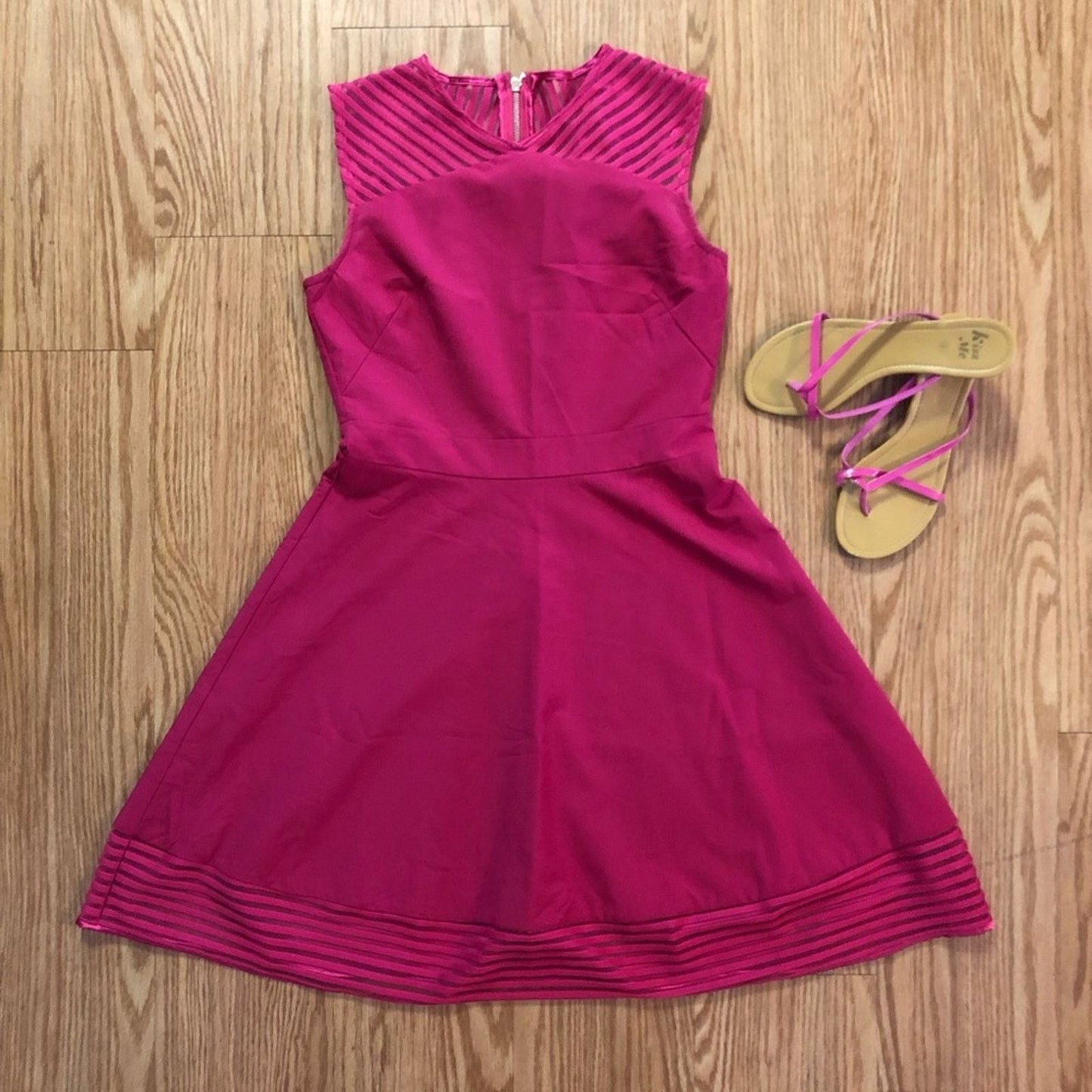 Pink sleeveless dress with sheer striped mesh panels on neckline and hem laid flat on wood floor