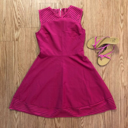 Pink sleeveless dress with sheer striped mesh panels on neckline and hem laid flat on wood floor